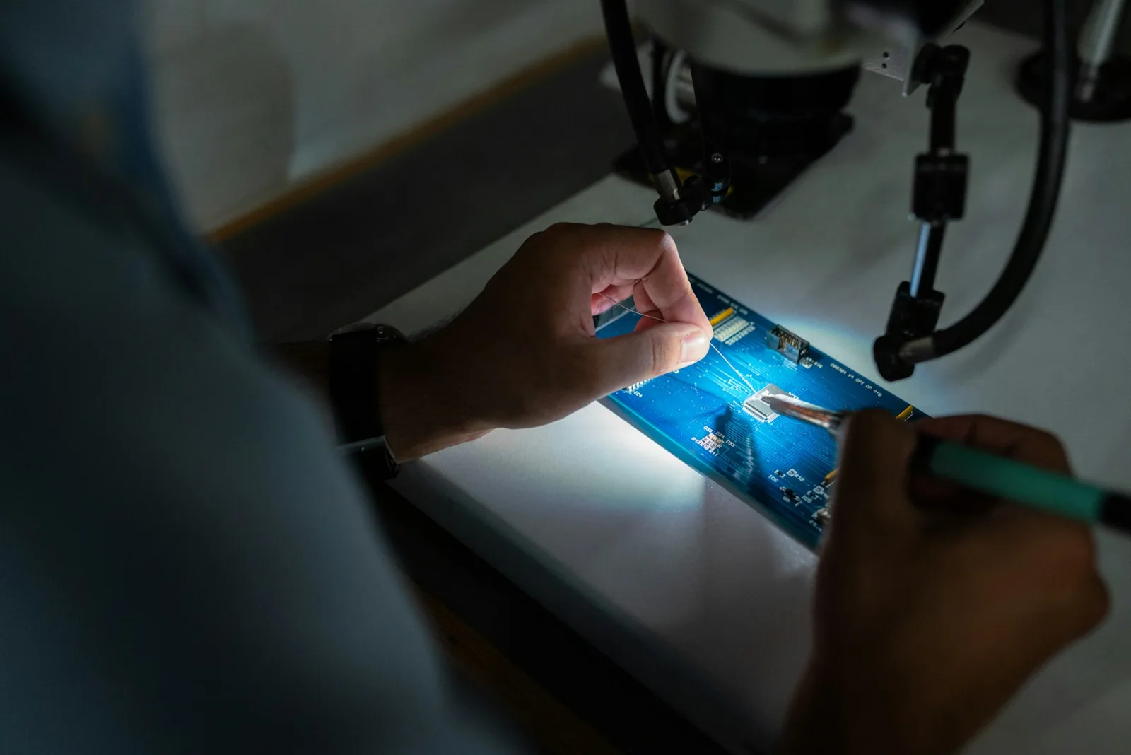 Hands testing an electronic circuit under a microscope